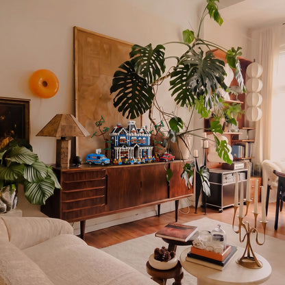 Brick-built Creel House from Stranger Things on a wooden sideboard beside a large monstera plant